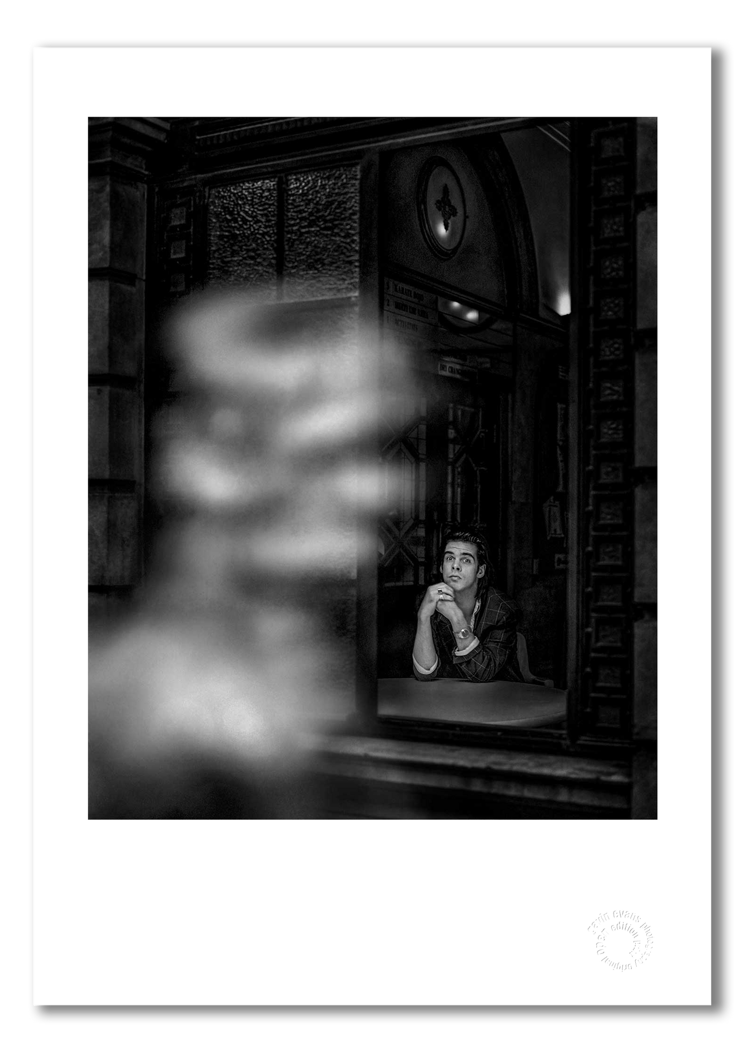 Black and white portrait of Nick Cave by Gavin Evans, 1989. Seated at window with blurred figure entering frame. A3 giclée print with white border, Nick Cave Collection.