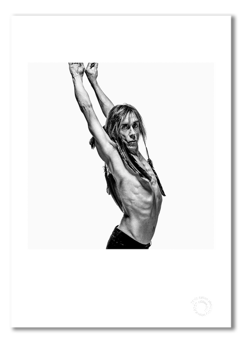 B&W profile portrait of Iggy Pop by Gavin Evans, 1996. Arms raised, crow feathers, head turned to camera. A3 giclée print with white border, Iggy Pop Collection.