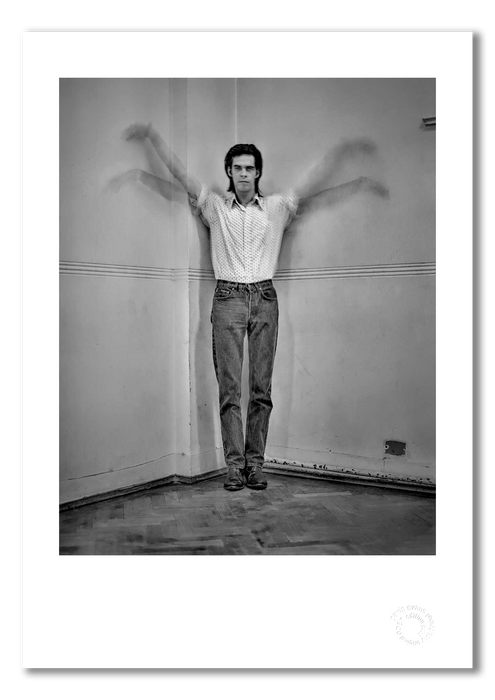 Black and white portrait of Nick Cave by Gavin Evans, 1989. Arms raised in bird-like motion, corner of tiled room. A3 giclée with white border, Nick Cave Collection.