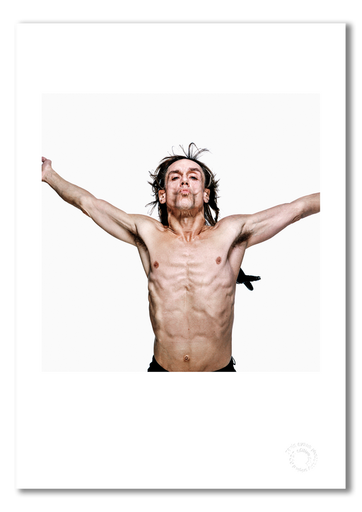 Colour studio portrait of Iggy Pop by Gavin Evans, 1996. Bare-chested, arms outstretched, black feathers, white background. A3 giclée with white border, Iggy Pop Collection.