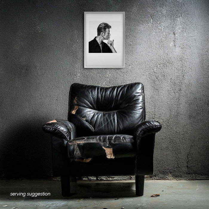 Framed B&W profile portrait of David Bowie by Gavin Evans, 1995. Shushing gesture. Displayed in dilapidated monochrome room, Bowie Collection.