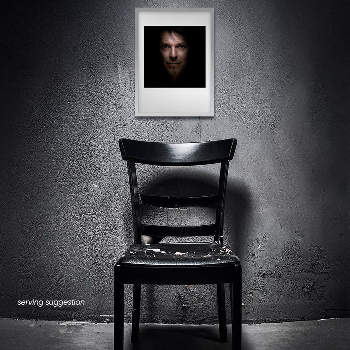 Framed colour headshot of David Bowie by Gavin Evans. Blue lenses, calm expression. Displayed in dilapidated monochrome room, Bowie Collection.
