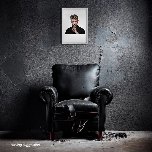Framed colour portrait of David Bowie by Gavin Evans. White background, shushing pose. Displayed in dilapidated monochrome interior, Bowie Collection.