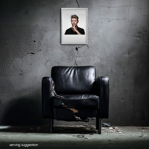 Framed colour shushing portrait of David Bowie by Gavin Evans. White background, off-camera expression. Displayed in dilapidated monochrome room, Bowie Collection