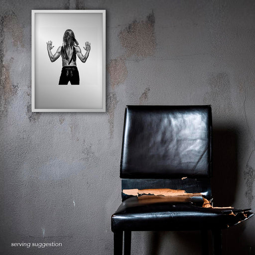 Framed B&W rear portrait of Iggy Pop by Gavin Evans, 1996. Back muscles and feather adornment, displayed in derelict setting, Iggy Pop Collection.