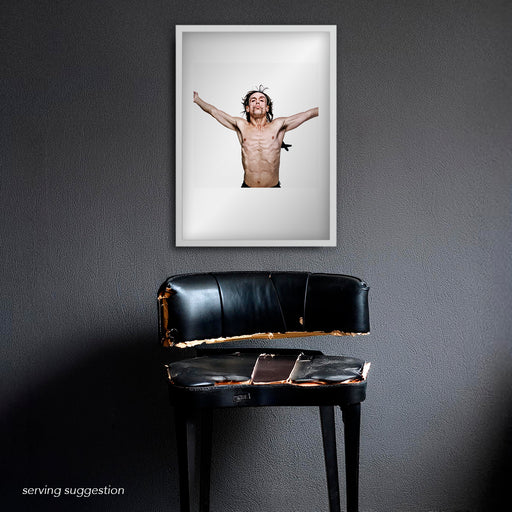 Framed Iggy Pop portrait by Gavin Evans, 1996. Bare torso, cruciform stance with feathers, hung against a monochrome wall, Iggy Pop Collection.