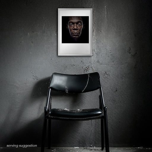 Framed display of the Maxi Jazz A3 fine art print in a distressed, textured interior. Emerging from deep black, the colour portrait radiates emotional clarity — a powerful contrast to the raw setting.