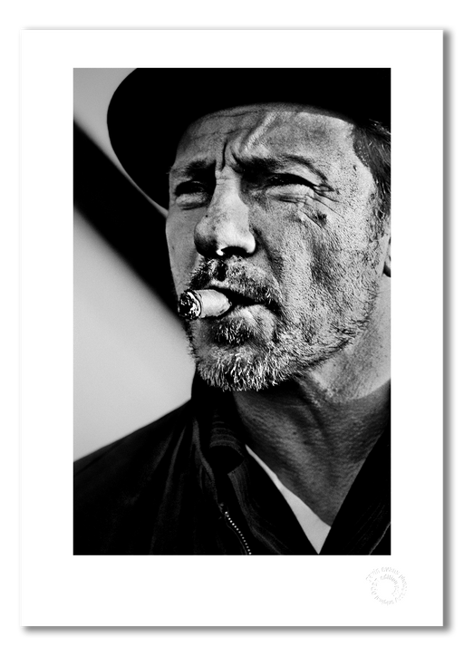 A3 open edition fine art print of Harvey Keitel smoking a cigar, featuring a white border and printed on semi-matt archival cotton paper. This 1986 black and white portrait by Gavin Evans is full of attitude and cinematic cool. Embossed for authenticity.