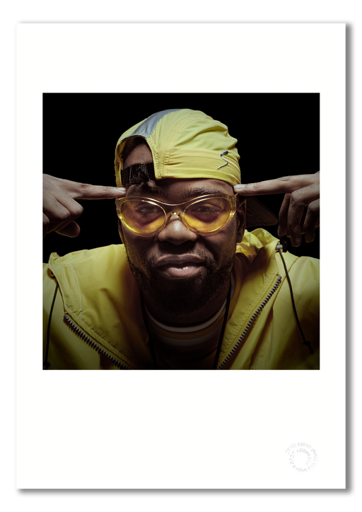 Colour portrait of Method Man by Gavin Evans, 1997. Yellow jacket, sunglasses, forefingers to temples. A3 giclée with white border, Icons Collection.