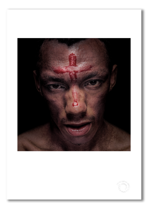 Colour close-up headshot of Tricky by Gavin Evans, 1996. Blood cross on forehead, emerging from black. Iconoclastic image, Icons Collection. Shown as A3 giclée print with white border, embossed for authenticity.